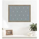 Framed blue botanical block print with evenly spaced small white leaf motifs on a textured background, hanging above a white shelf with a lamp, photo frame, and potted plant.