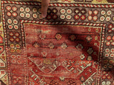Close-up of a distressed antique Turkish wool prayer rug with a red central field and intricate floral and geometric motifs in cream, brown, and rust colors with visible wear and fading.