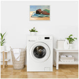 Framed canvas depicting a woman in a green top lying on a blue-and-white striped towel at the beach, displayed above a white front-loading washing machine.