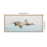 Framed canvas print of two cranes flying closely against a pale sky, measuring 40 by 18 inches with a thin wooden frame.