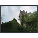 Framed canvas showing a cloudy mountain ridge with jagged rock formations and lush green meadows, with a winding trail visible on the right side.