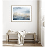 Abstract horizontal painting with tonal blue, gray, and beige brushstrokes evoking an oceanic atmosphere in a simple wood frame hanging above a wooden bench with white fabric