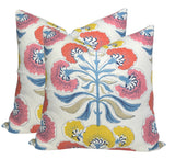 Two square pillows with white background featuring a coral, yellow, and blue floral tree motif with stylized petals and curved leaves.