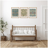 Three framed Sylvie William Morris botanical-style prints with intricate floral patterns in muted green, blue, and beige tones above a wooden bench with white cushions in a minimalist room.