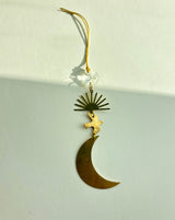 Hanging ornament with a gold crescent moon, a small bird above it, a fan-shaped sunburst, and a clear vintage glass crystal at the top, suspended by a yellow string.
