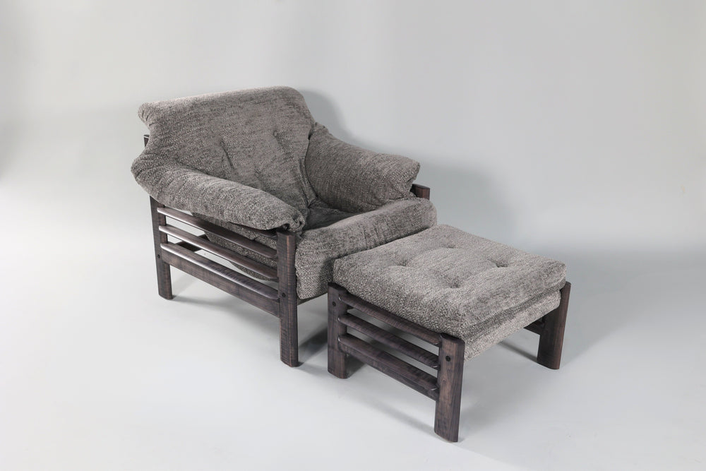 Black stained wooden chair with thick gray tufted cushions and matching ottoman featuring horizontal slat sides, shown angled on a light background.