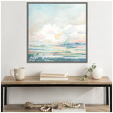 Square framed watercolor landscape painting with soft blues, greens, and pinks above a wooden console table holding a white mug, stacked books, and a white vase with a trailing plant.