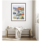 Abstract landscape painting with layered geometric shapes in blue, orange, and green hues, framed in wood and hanging above a woven bench with a draped cream blanket.