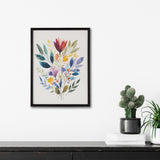 Framed watercolor botanical bouquet with jewel-toned leaves and flowers in reds, blues, yellows, and greens, hanging above a black surface with two potted plants and stacked white books.