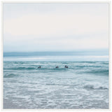 Three surfers sitting on surfboards in calm ocean waves under a pale, overcast sky in a square framed canvas print.