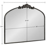 Arched mirror with a dark metal frame topped by an ornate carved decorative crest, measuring 36 inches wide and 28.5 inches tall.