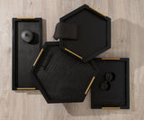 Set of four black wooden trays with gold handles in rectangular, hexagonal, and square shapes, arranged on a light wood floor with minimal decoration inside.