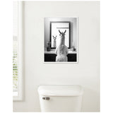 Black and white photo of a llama looking into a rectangular mirror, framed by two small potted plants on a bathroom counter, against a white wall above a toilet tank.