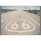 Framed canvas showing a straight desert highway with Route 66 emblem painted on the road, flanked by arid landscape and distant mountains under a clear sky.