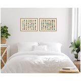 Two framed abstract canvases above bed with white linens featuring colorful evenly spaced circular dots in green, orange, blue, and gold hues, flanked by green plants.