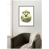 Framed canvas wall art of a hedgehog composed of green and white flowers with black eyes and nose, hanging above a dark green armchair draped with a cream knit blanket.