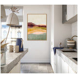 Abstract landscape artwork featuring layered hues of burgundy, peach, mustard, and green in soft gradients, framed and hung on a white wall in a modern kitchen.