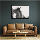Black and white close-up photo of a horse's face with flowing mane in a black frame, hanging on a dark green wall above a brown leather sofa and wooden coffee table.