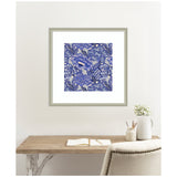 Square artwork featuring dense blue and white floral patterns with intricate line details, framed in light gray and hung above a wooden desk with white accents.
