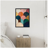 Abstract geometric artwork with overlapping semicircles in jewel tones like teal, orange, and pink, framed in black and hung on a white wall above a wooden block side table.
