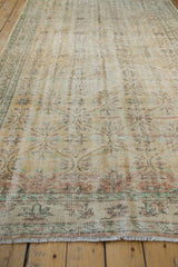 Vintage distressed Oushak carpet in faded beige and muted teal with floral motifs and border, laid on a wooden floor.