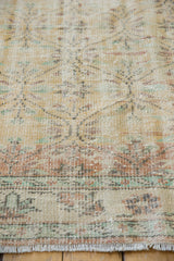 Close-up of a vintage distressed Oushak carpet featuring muted beige background with faded pastel blue and soft rust geometric floral patterns and worn fringed edge.