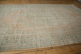 Rectangular vintage Oushak carpet in muted beige and pale blue with a distressed, faded pattern lying flat on a wooden floor.