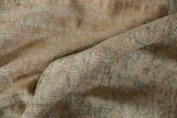 Close-up of a vintage distressed Oushak carpet with muted beige and brown tones, showing a folded section revealing its textured woven pattern.
