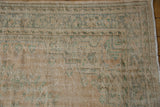 Section of a vintage distressed Oushak carpet in muted beige with faded green and blue decorative floral border patterns on textured weave.