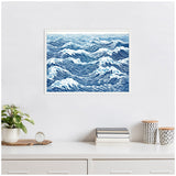 Framed linocut artwork depicting abstract blue and white ocean waves with intricate flowing lines, hung on a white wall above a minimalist desk with plants and decor.