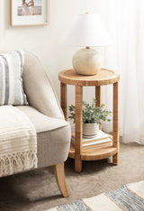 Round side table with woven texture, natural wood color, holding a beige spherical lamp and a small potted plant on the lower shelf, next to a light beige sofa.