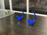 Two glossy cobalt blue bird-shaped figurines with elongated curved tails placed on a dark wooden surface with a carved feather pattern.