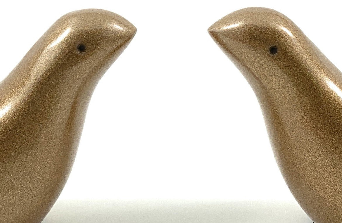 Close-up of two golden-brown bird figurines facing each other with smooth, metallic textured surfaces and small black eyes on a white background.