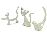 Three silver ring holders shaped like a dog with raised tail, a sitting cat with upright tail, and a bird with a tall curved tail, all smooth and shiny.