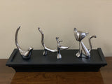 Set of four sleek silver ring holders shaped like a bird, dog, cat, and standing figure, displayed on a black rectangular tray on a wooden surface.