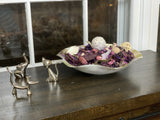 Silver-toned animal ring holders shaped as an elephant and a cat on a dark wooden surface next to a shallow bowl filled with assorted dried purple and beige potpourri.