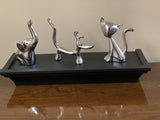 Three silver animal-shaped ring holders—a dog, elephant, and cat—arranged on a black rectangular tray on a wooden surface against a beige wall.
