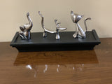 Silver ring holders shaped as an elephant, dog, deer, and cat arranged on a rectangular black tray on a wooden surface.