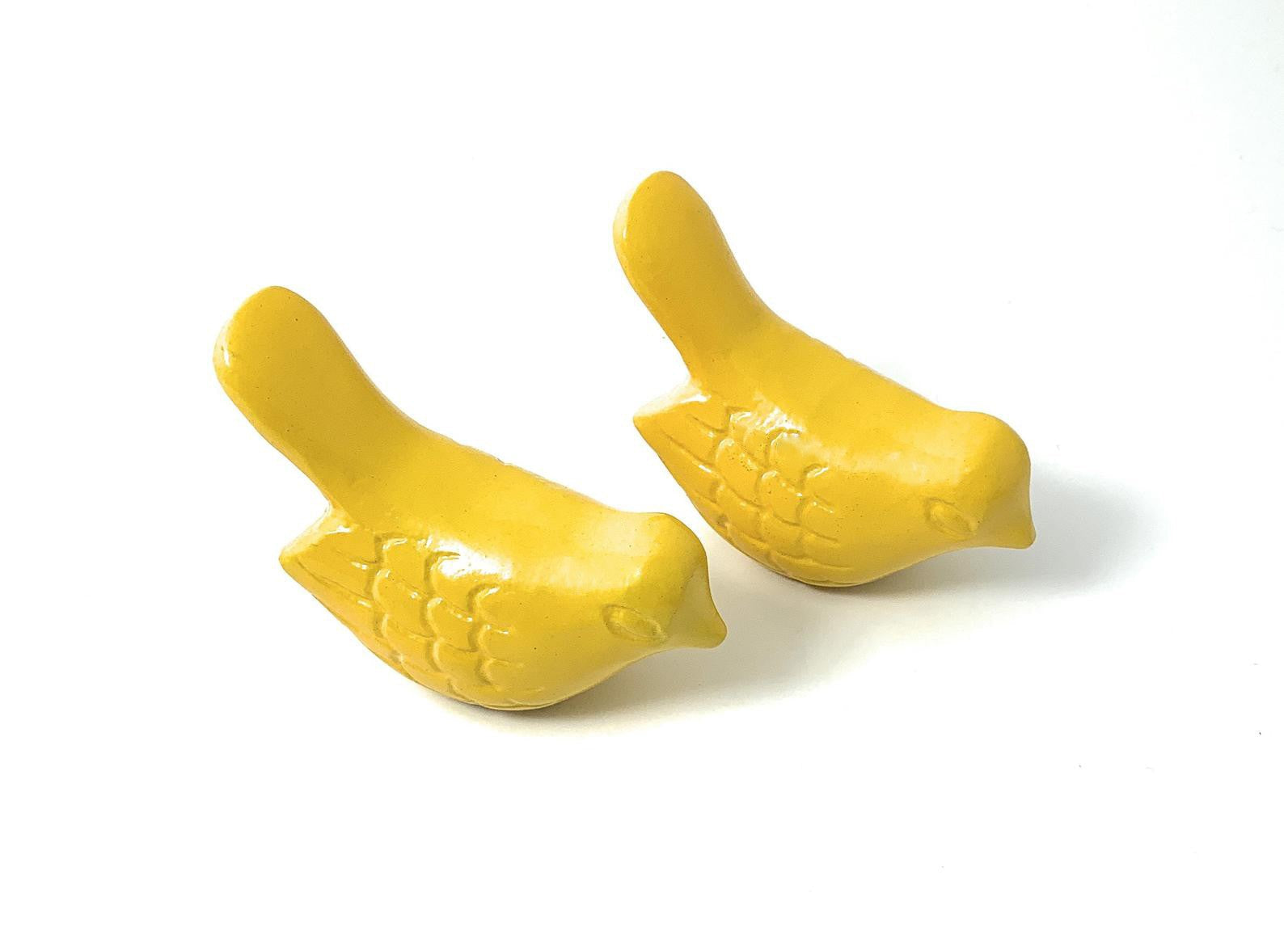 Two yellow handcrafted bird figurines side by side on a table surface