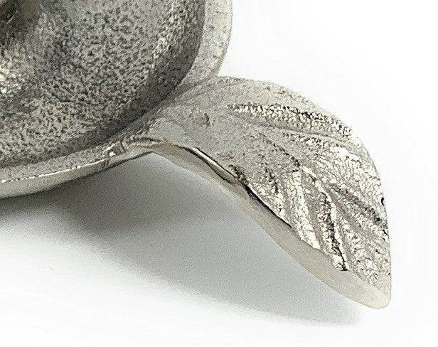 Close-up of a silver candlestick holder dish with a textured leaf-shaped handle extending from its round base.