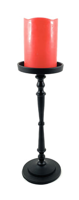 Matte black pillar candle holder with a turned, decorative stem holding a thick, vibrant red candle with scalloped top edge.