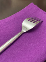 Silver-toned salad appetizer fork with hammered textured handle and 'Vibhsa' engraving, placed on a vibrant purple fabric background.