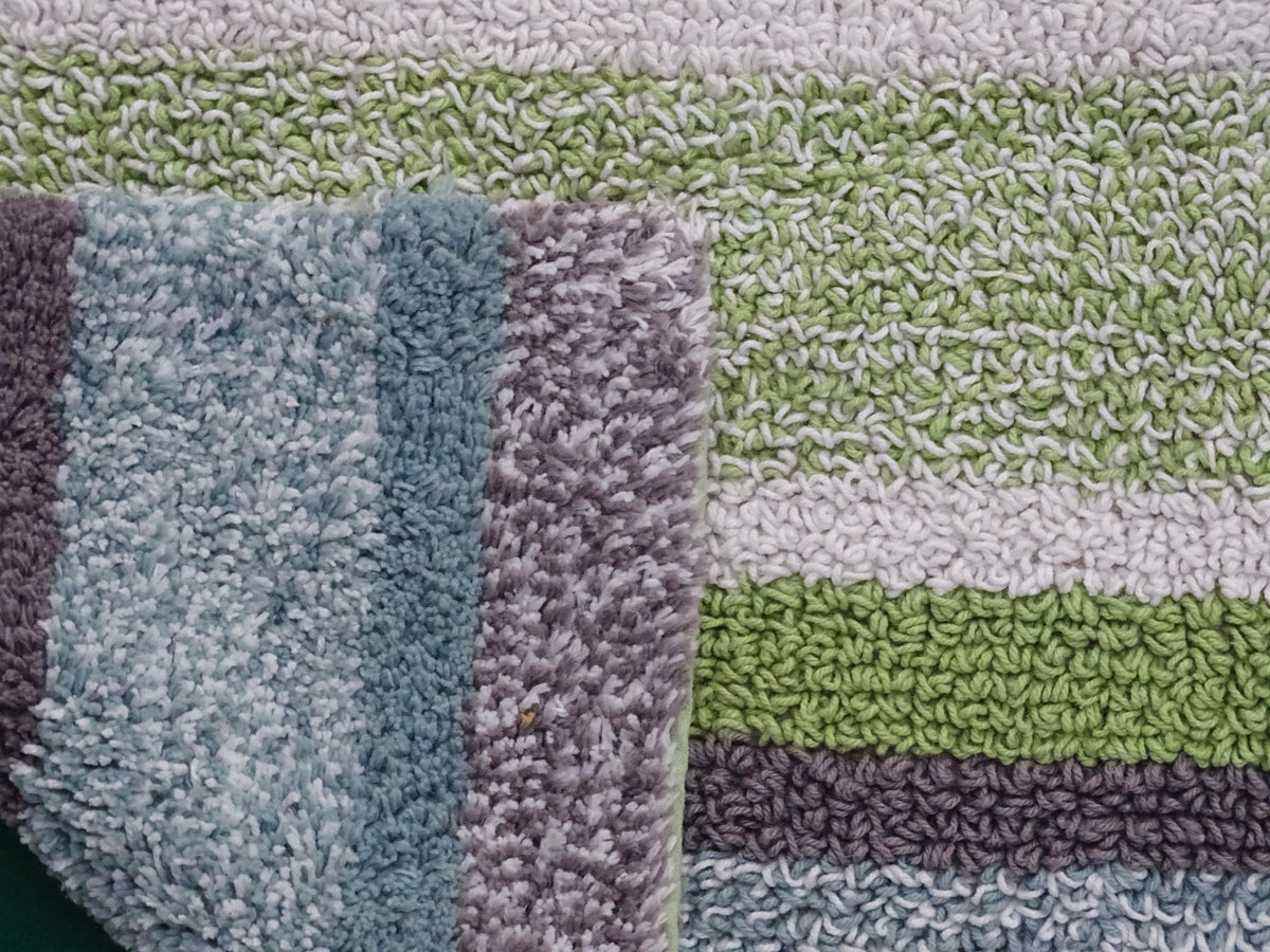 Close-up of a multi-color striped bath rug with textured loops, featuring stripes in shades of light blue, green, white, purple, and gray.