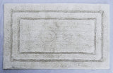 Rectangular ivory bath rug with a subtle raised pattern of two concentric rectangles near the edges on a light blue background.