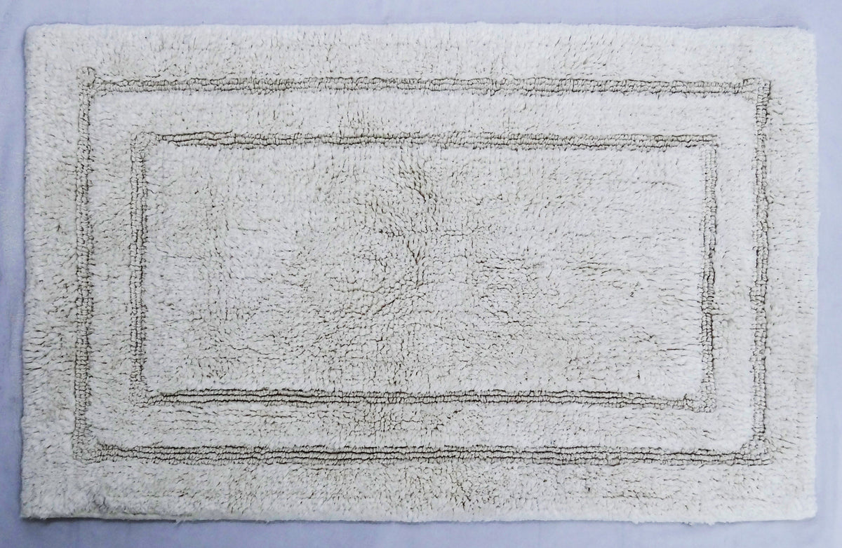 Rectangular ivory bath rug with a subtle raised pattern of two concentric rectangles near the edges on a light blue background.