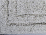 Close-up view of a plush ivory bath rug with a raised rectangular border pattern and a textured, fluffy surface.