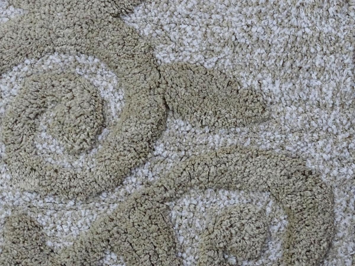 Close-up of a beige and ivory bath rug featuring a textured damask pattern with intertwined swirls and curves.