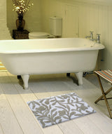 White clawfoot bathtub on light wood floor with beige and ivory damask patterned bath rug in front and a striped folding chair to the right