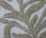 Close-up of a bath rug with a beige damask pattern on an ivory background, showing textured loops and raised design details.