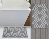 Rectangular bath rug with a grey background and ivory geometric zigzag diamond pattern, shown laid flat and hanging vertically in a bathroom setting.